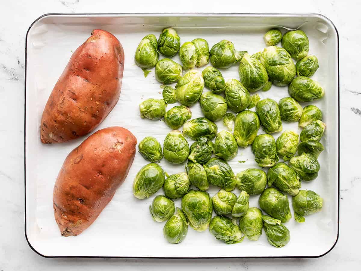 Prepped sweet potatoes on the baking sheet with Brussels sprouts