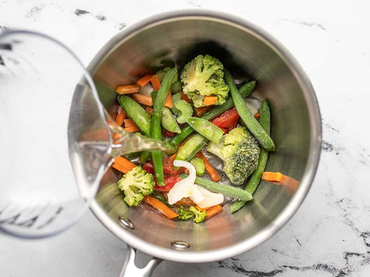 water pouring into a saucepot with frozen vegetables