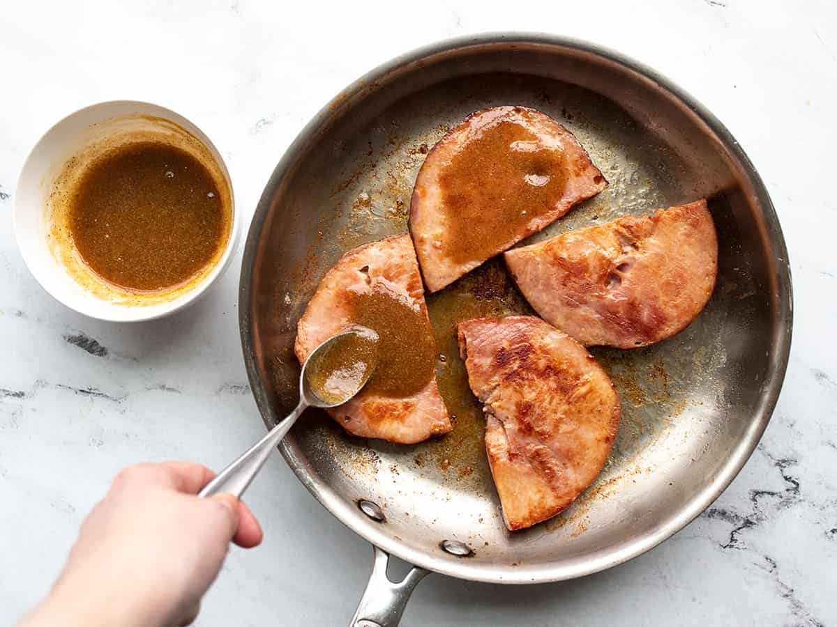 Glaze being spooned over the ham steaks in the skillet