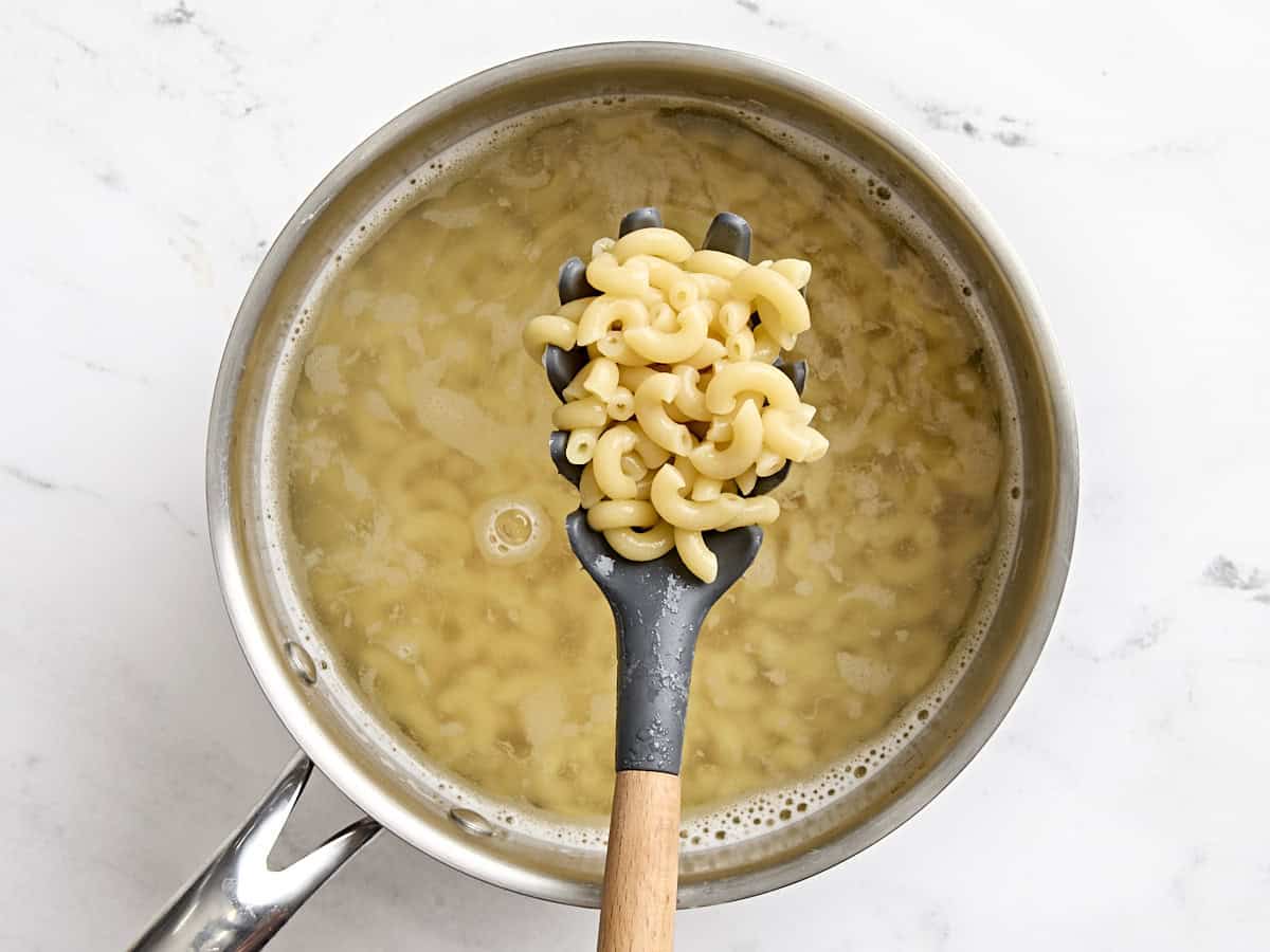 Boiled macaroni pasta on a slotted spoon.