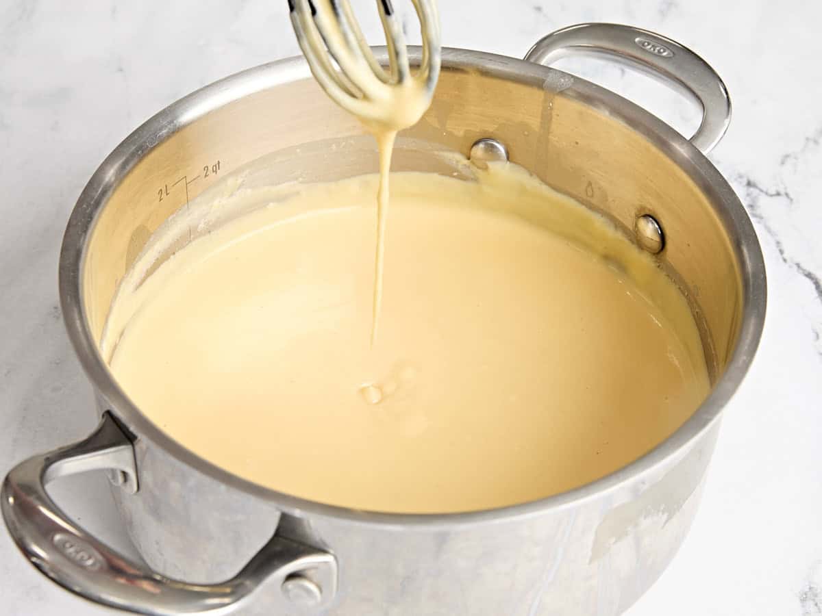 A whisk dipped into the creamy sauce for mac and cheese.