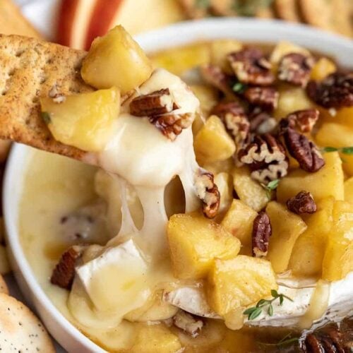 close up of a cracker dipping into the baked brie with cheese pull