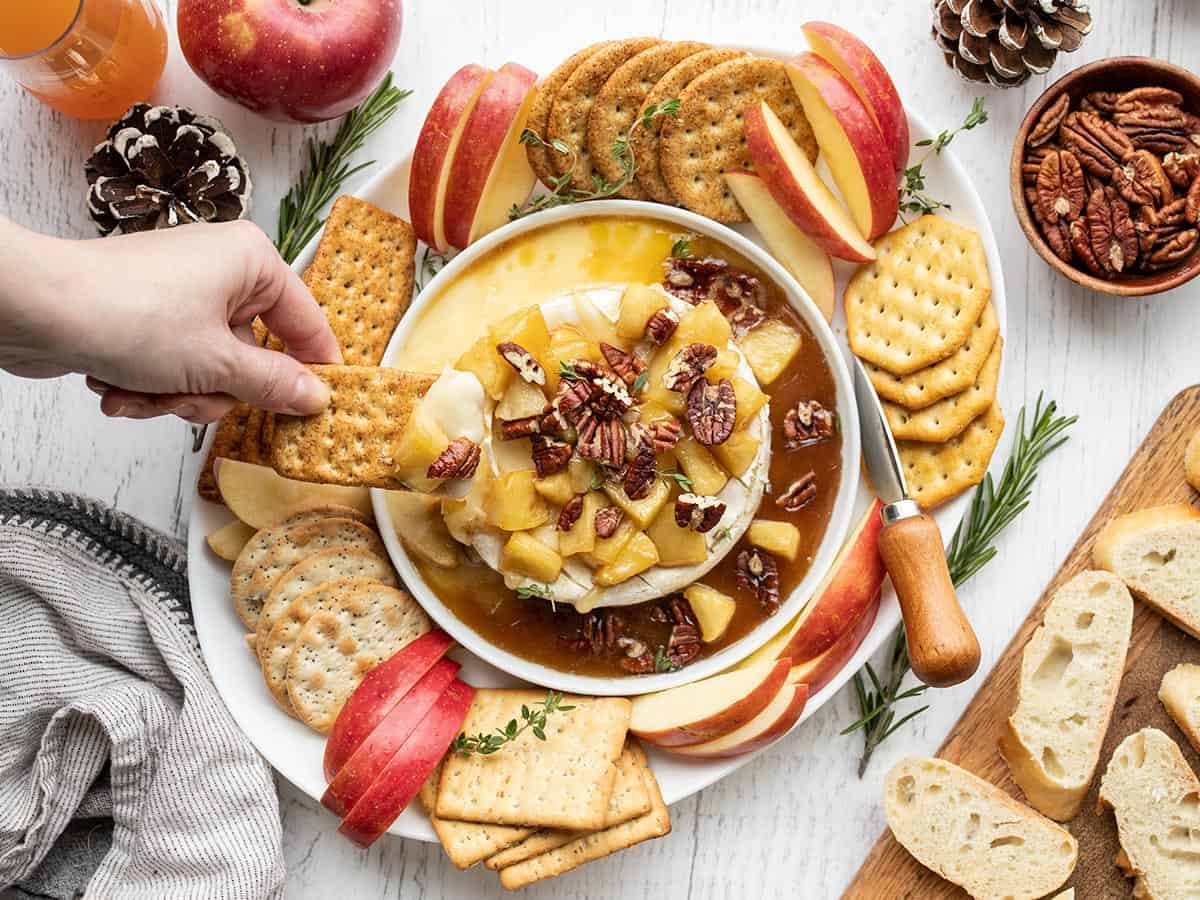 A hand dipping a cracker into the baked brie