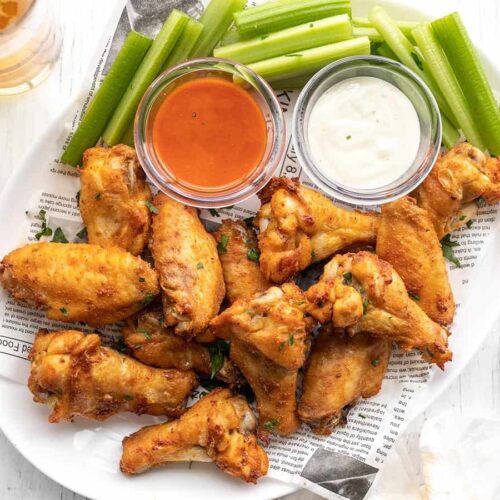 A platter full of baked chicken wings, celery, and two dipping sauces