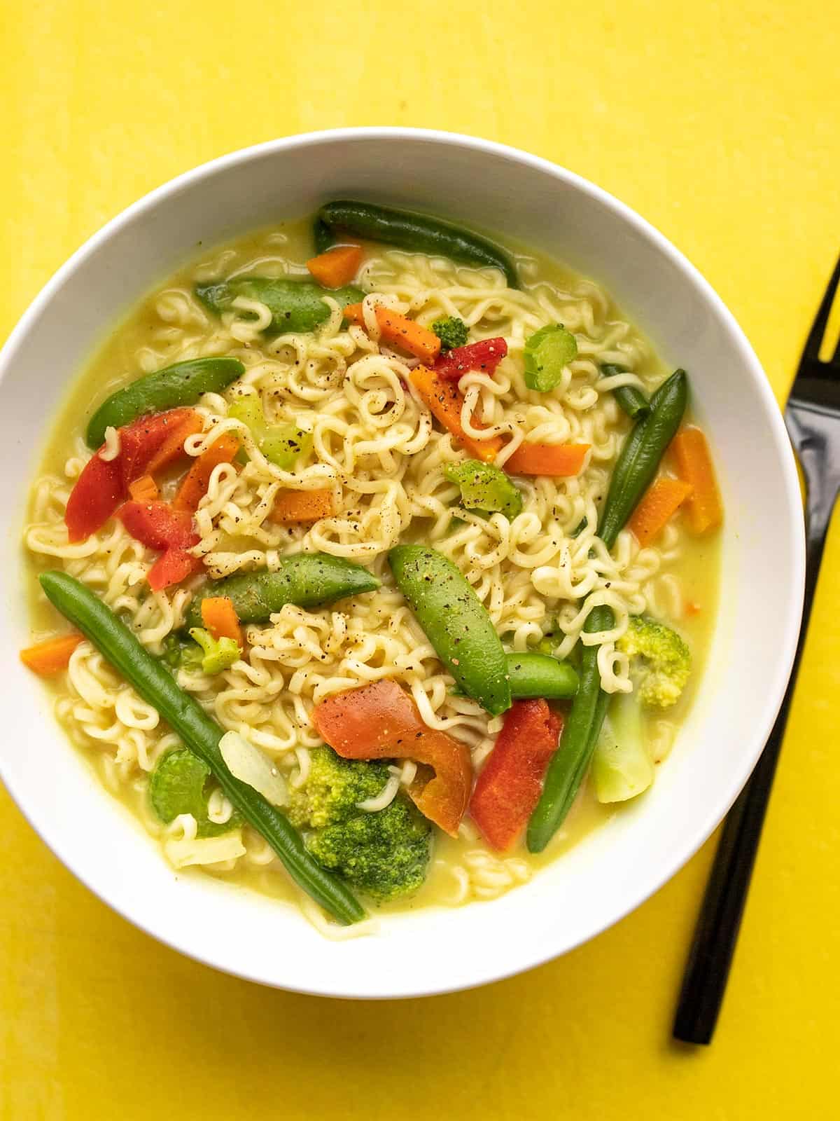 Overhead view of a bowl of coconut curry ramen on a yellow background