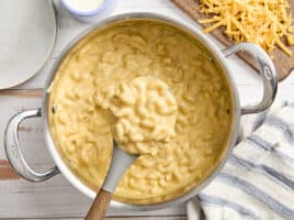 Overhead view of mac and cheese in a sauce pan, with some on a serving spoon.