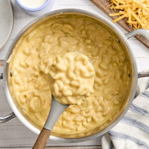 Overhead view of mac and cheese in a sauce pan, with some on a serving spoon.