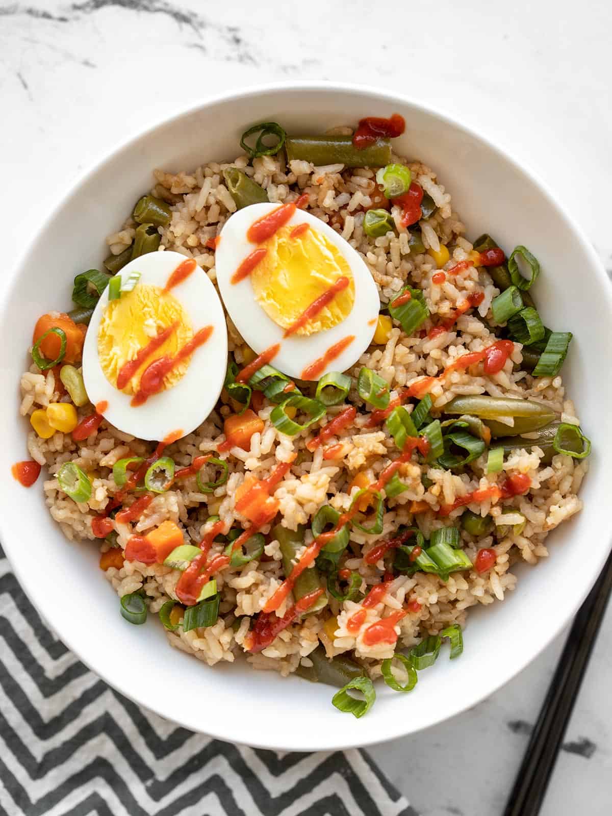 overhead view of veggie and rice bowl topped with sriracha