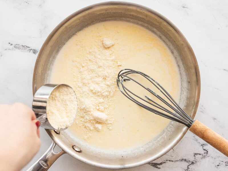 Parmesan being added to the cream in the skillet.