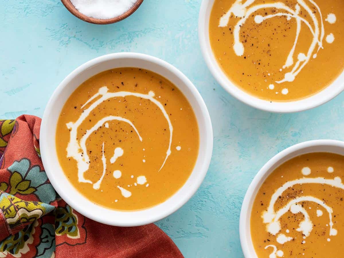 Three bowls of creamy sweet potato soup on a blue background