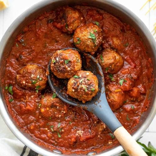 Meatballs in a pot of red sauce with a spoon holding two meatballs