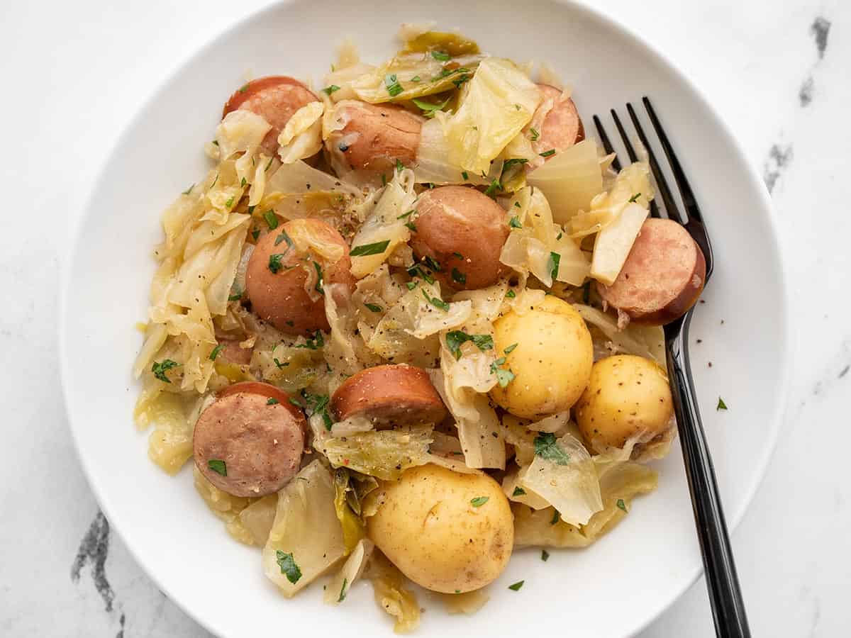 slow cooker cabbage and sausage in a shallow bowl with a fork