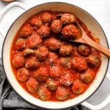 Overhead view of homemade meatballs in a skillet with marinara sauce and a spoon.