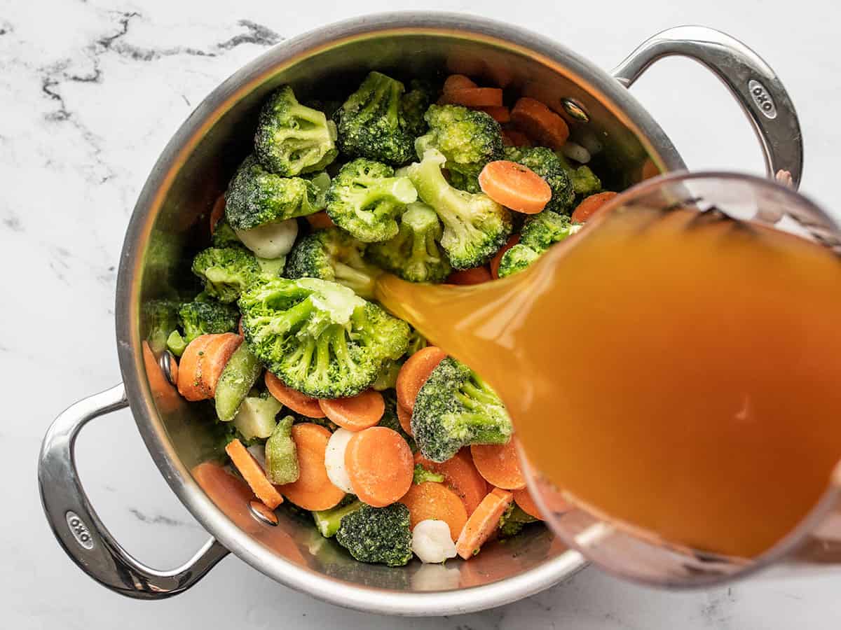 broth being poured into a pot with frozen vegetables