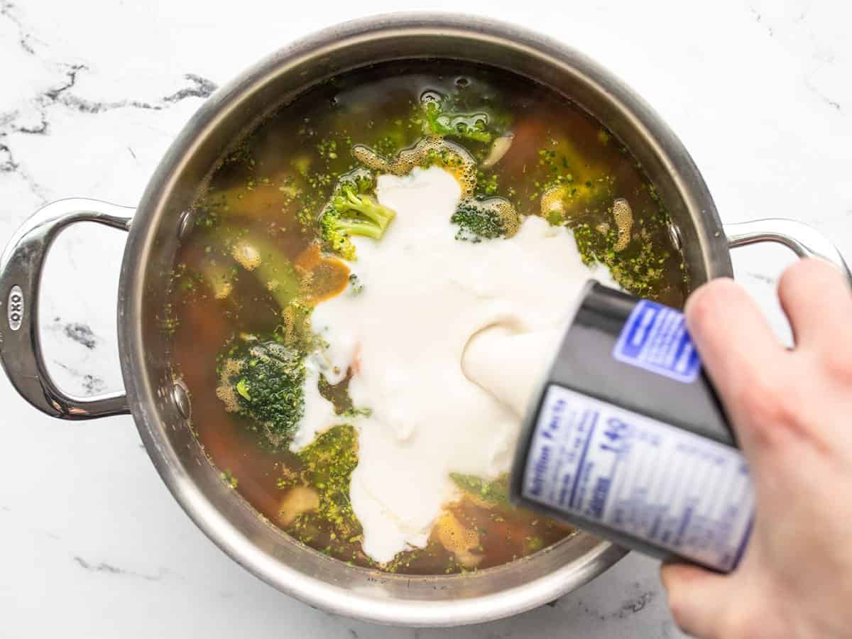 Coconut milk being poured into the pot with broth and vegetables