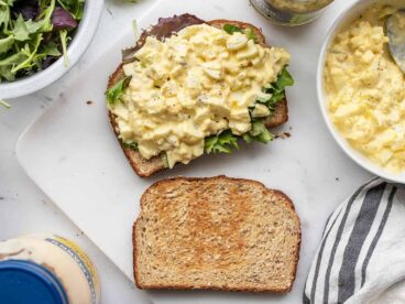 An egg salad sandwich being built on a cutting board