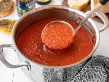 A ladle full of roasted red pepper soup being lifted from the pot