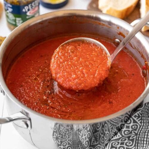 A ladle full of roasted red pepper soup being lifted from the pot