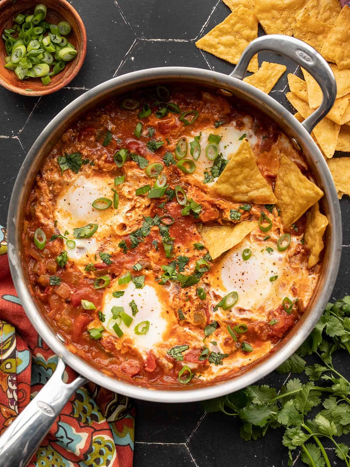 salsa poached eggs in a skillet with tortilla chips and green onion on the sides