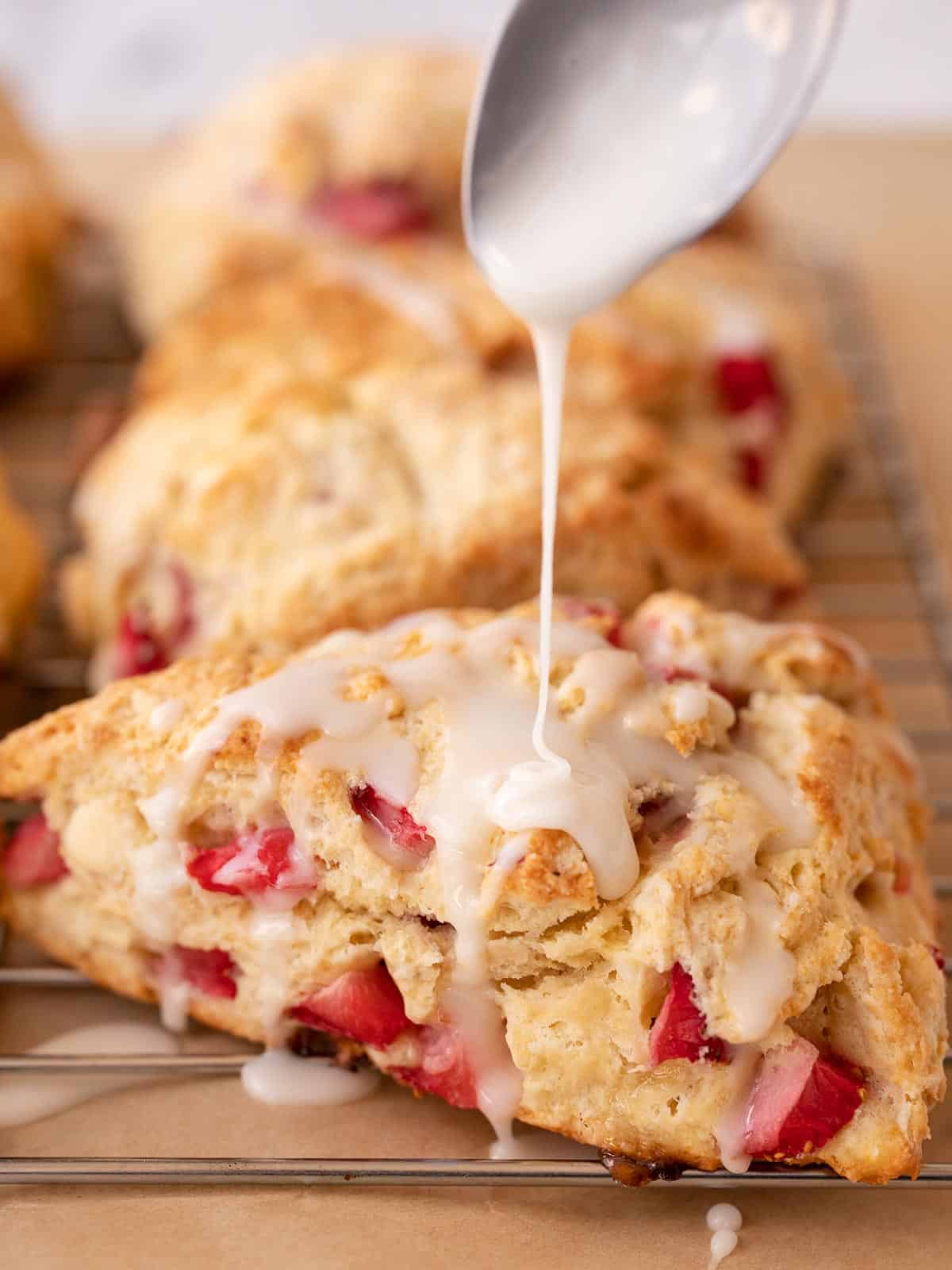 Close up of glaze being drizzled over a strawberry scone