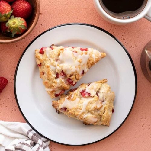 Two strawberry scones on a plate with coffee and a bowl of berries on the side