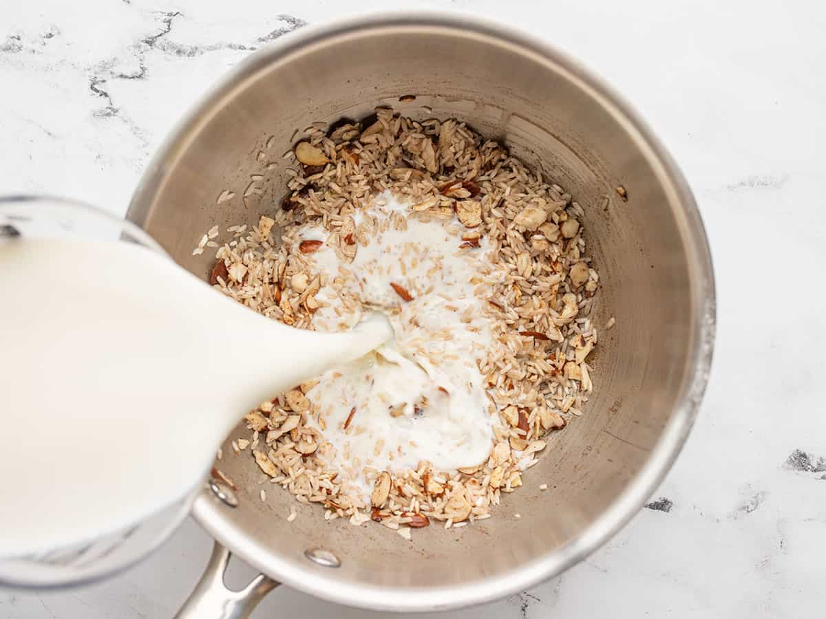 Milk being poured into the pot with rice, almonds, and spices.