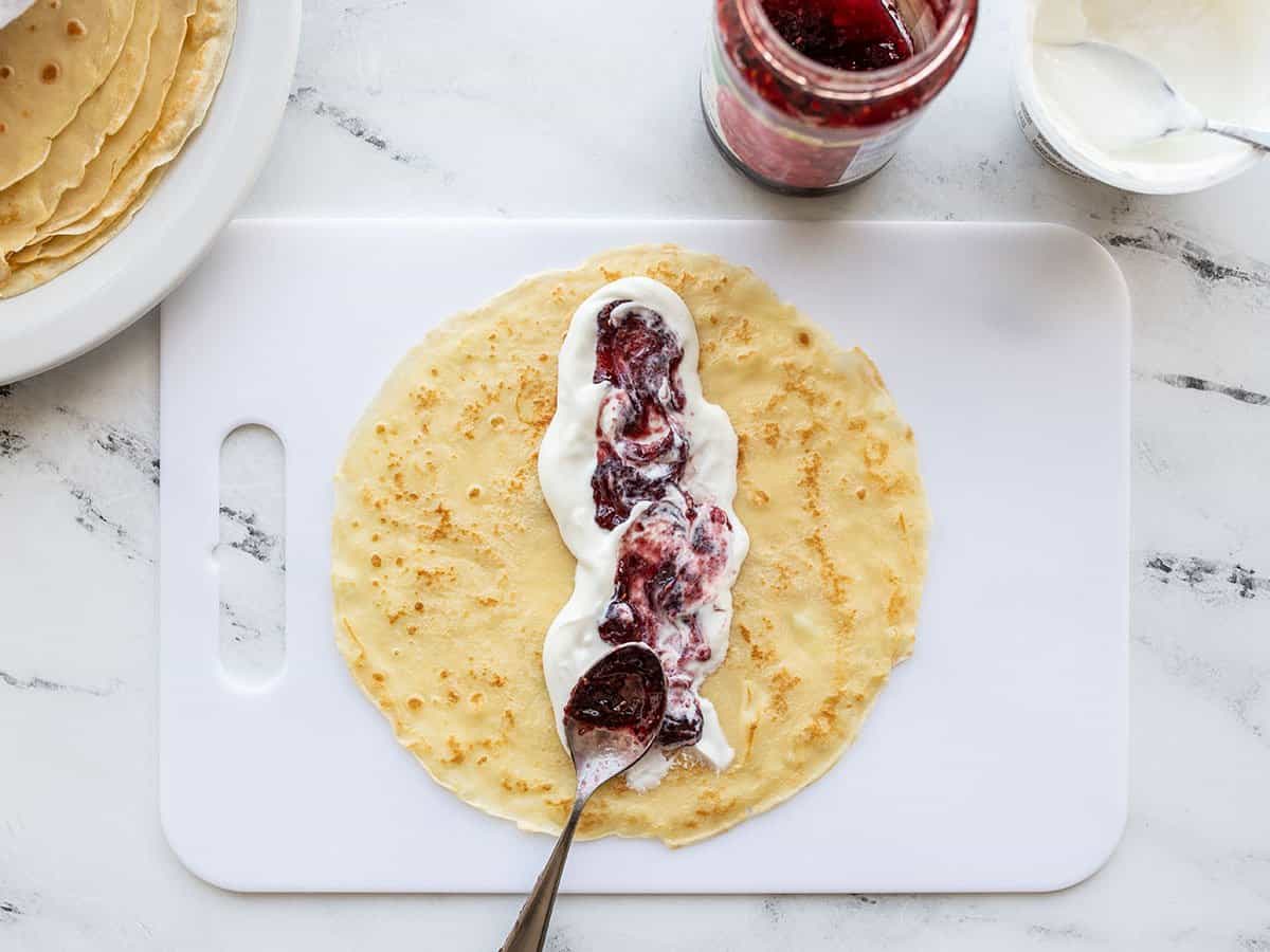 yogurt and jam being spread on the center of a crepe.