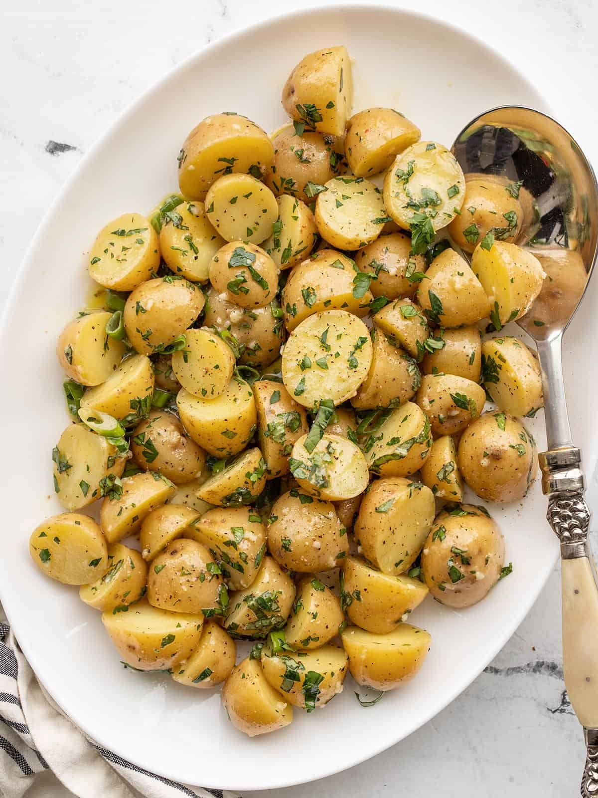 overhead view of an oval platter full of herby potato salad.