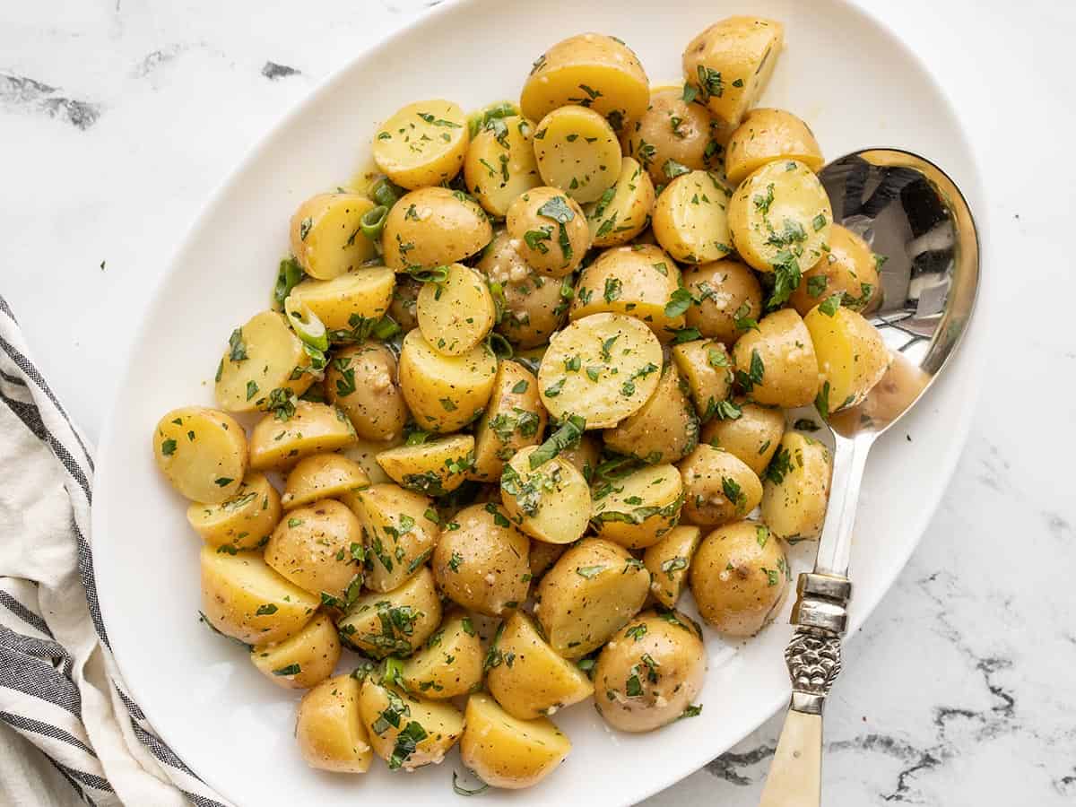 Overhead view of a platter full of potato salad with a fancy serving spoon. 