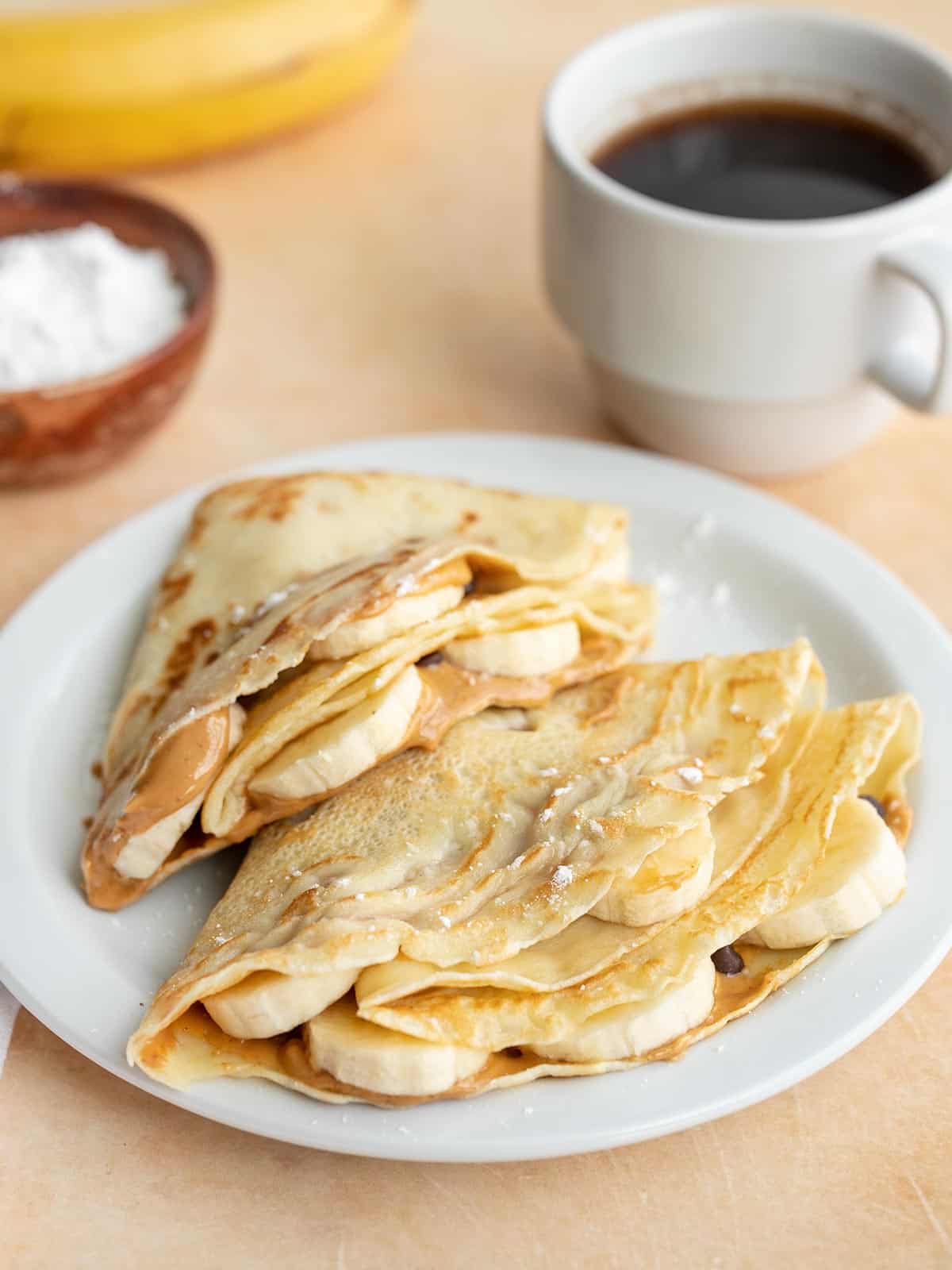 Two folded crepes on a plate stuffed with peanut butter and bananas