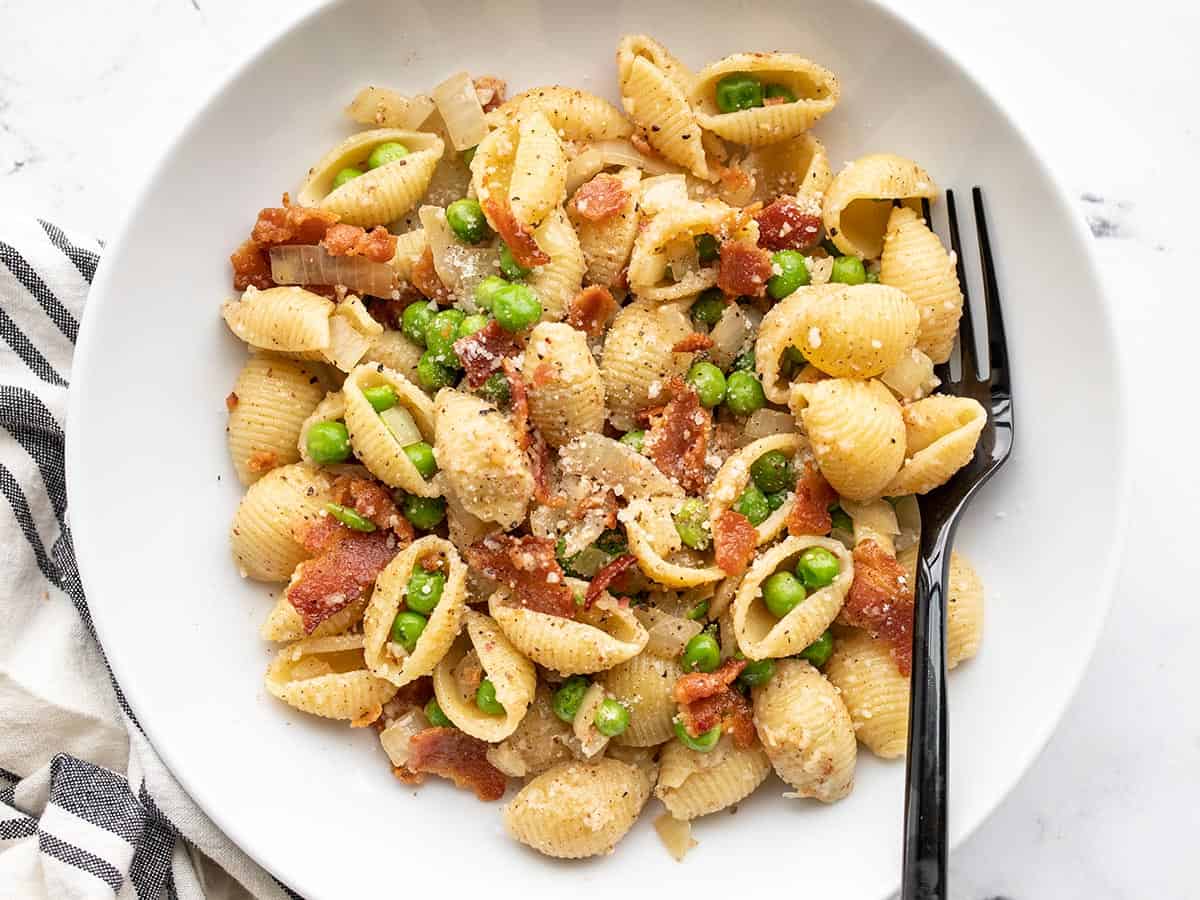 Close up overhead view of a bowl of pasta with bacon and peas.