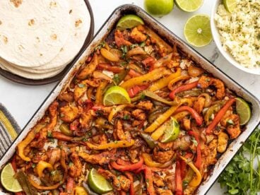 Sheet pan full of chicken fajitas with rice and tortillas on the side