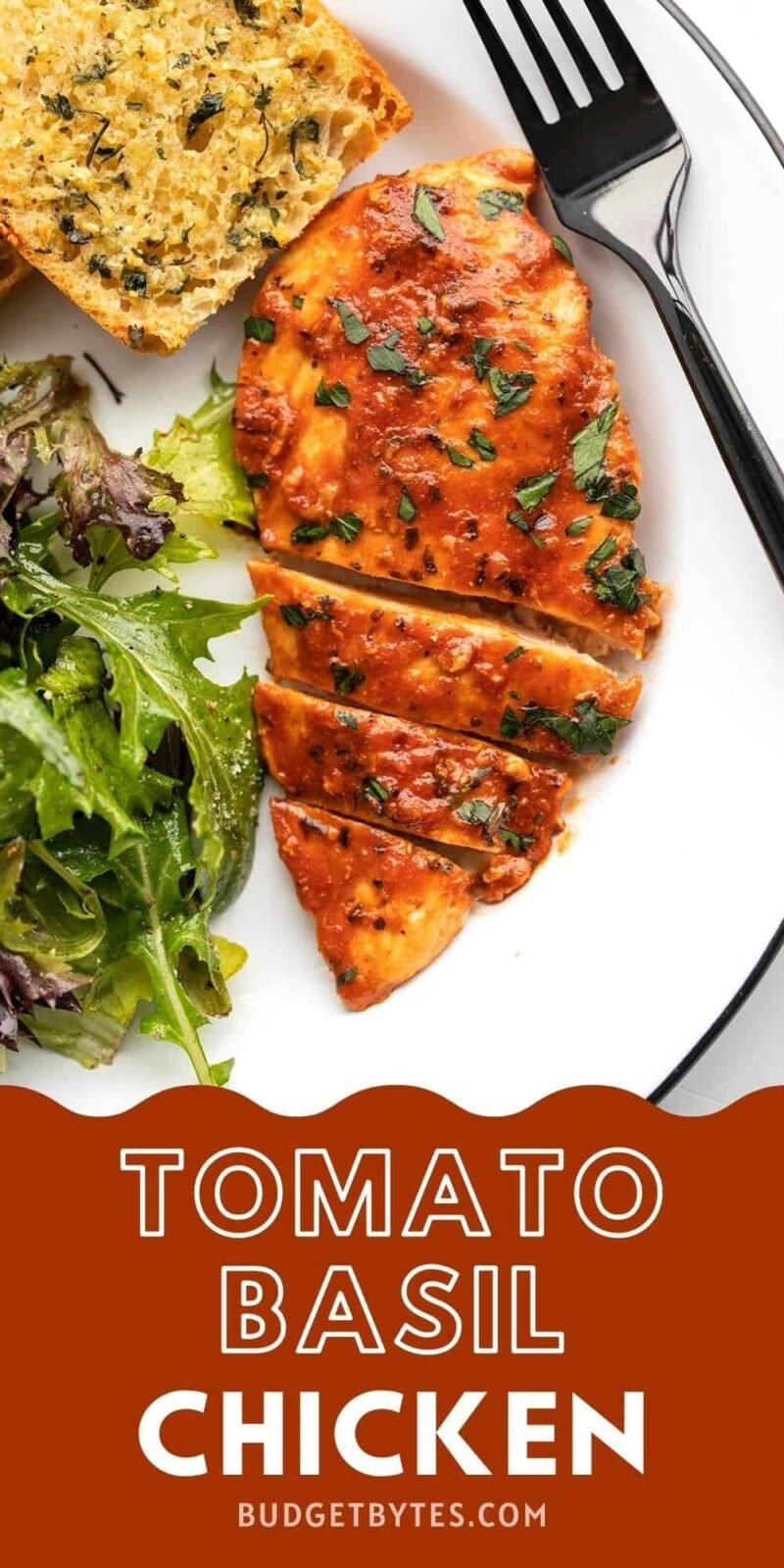 sliced tomato basil chicken breast on a plate with salad and garlic bread