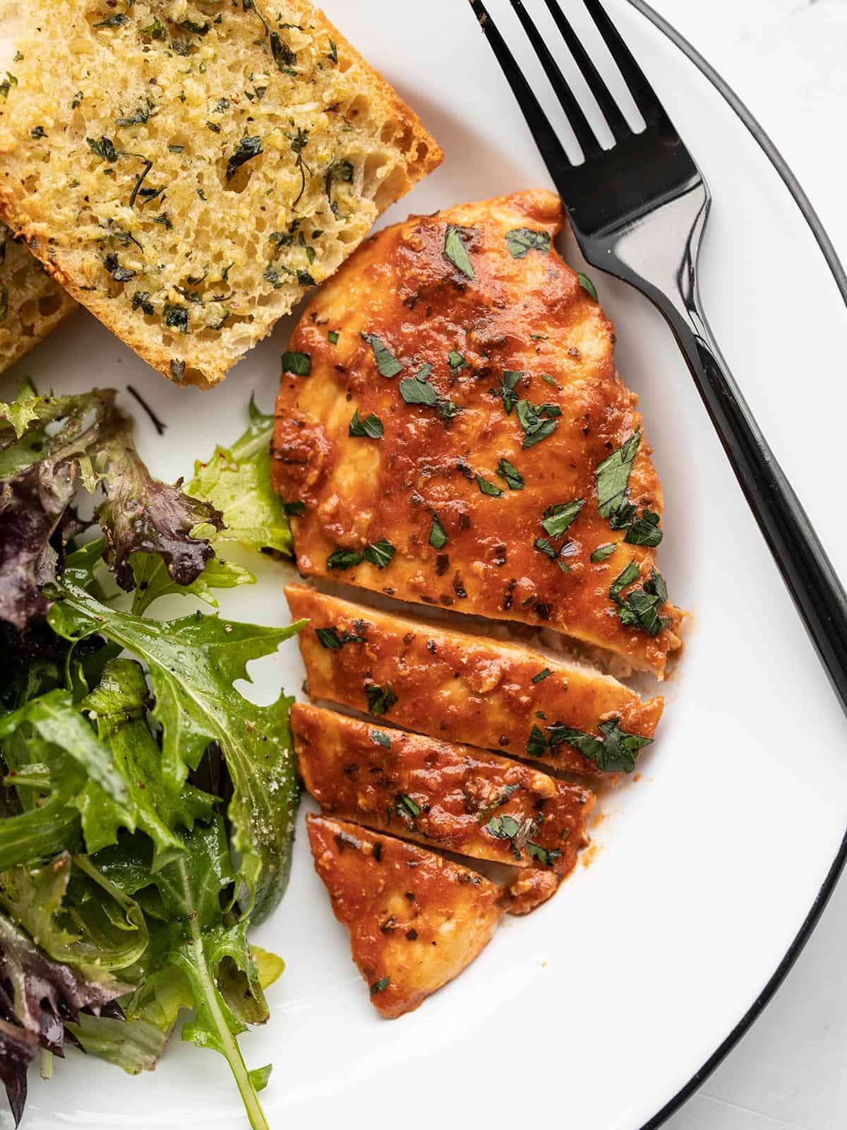 A sliced tomato basil chicken breast on a plate with garlic bread and a salad