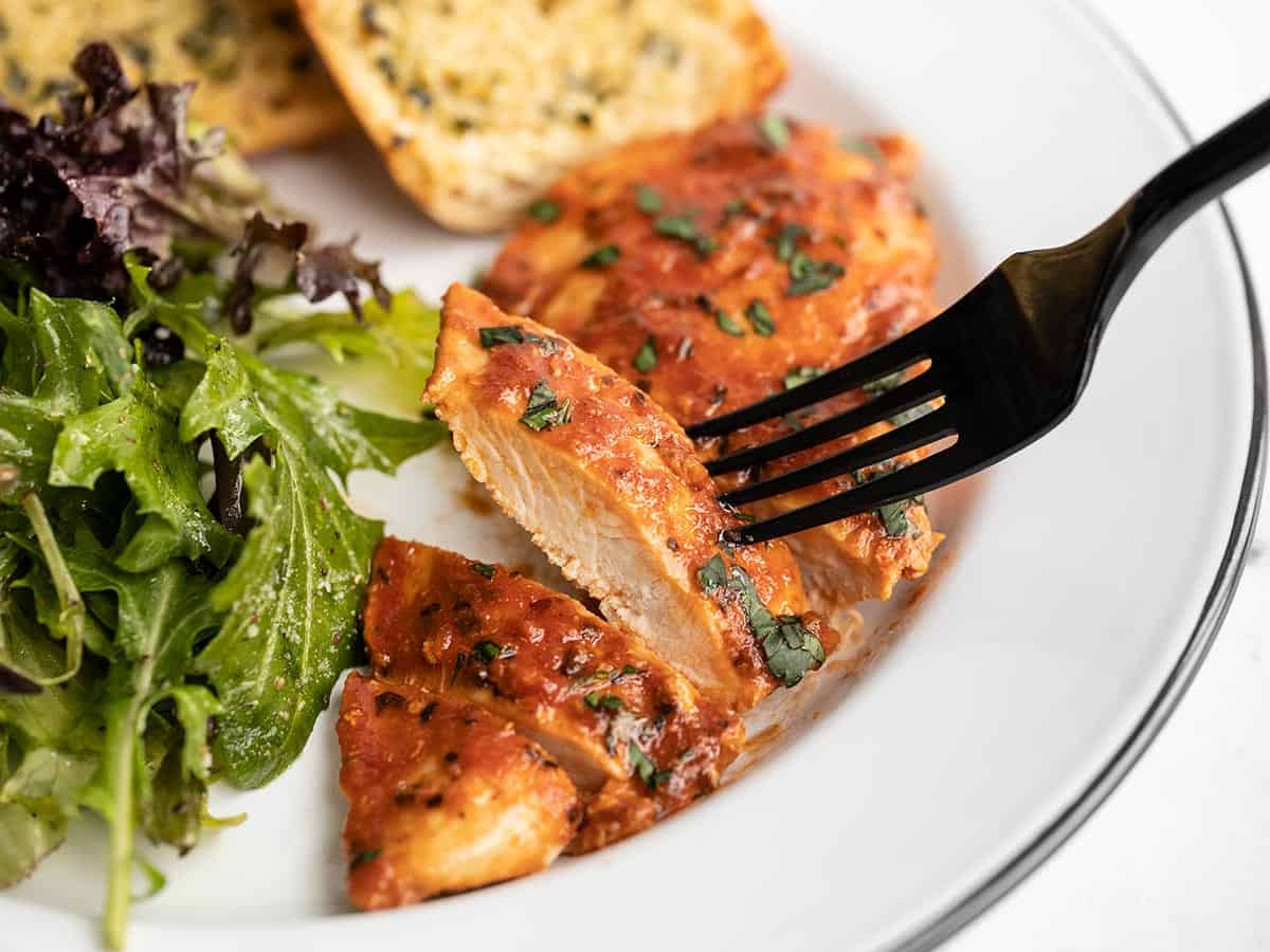 A fork lifting a sliced piece of tomato basil chicken off the plate