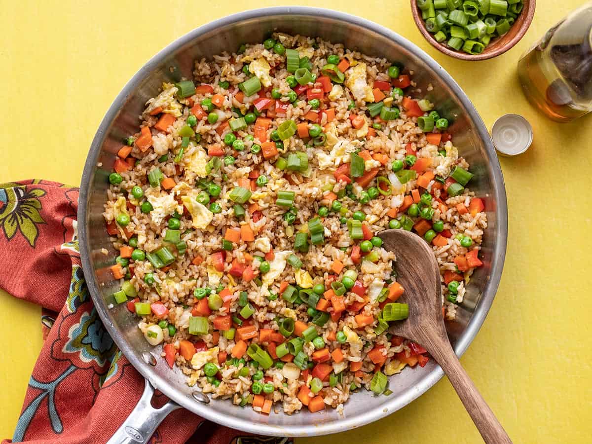 Overhead view of fried rice in a skillet with a wooden spoon.