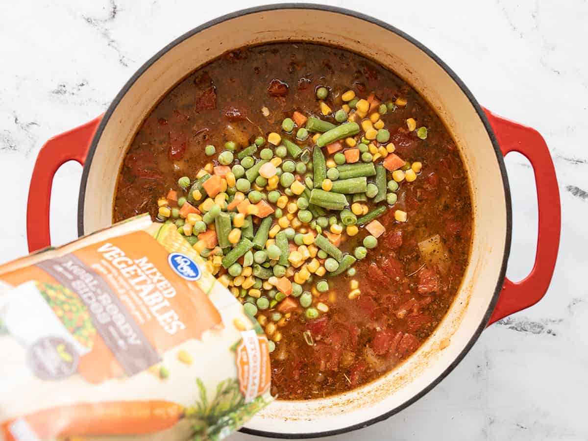 Frozen vegetables being poured into the pot of soup.