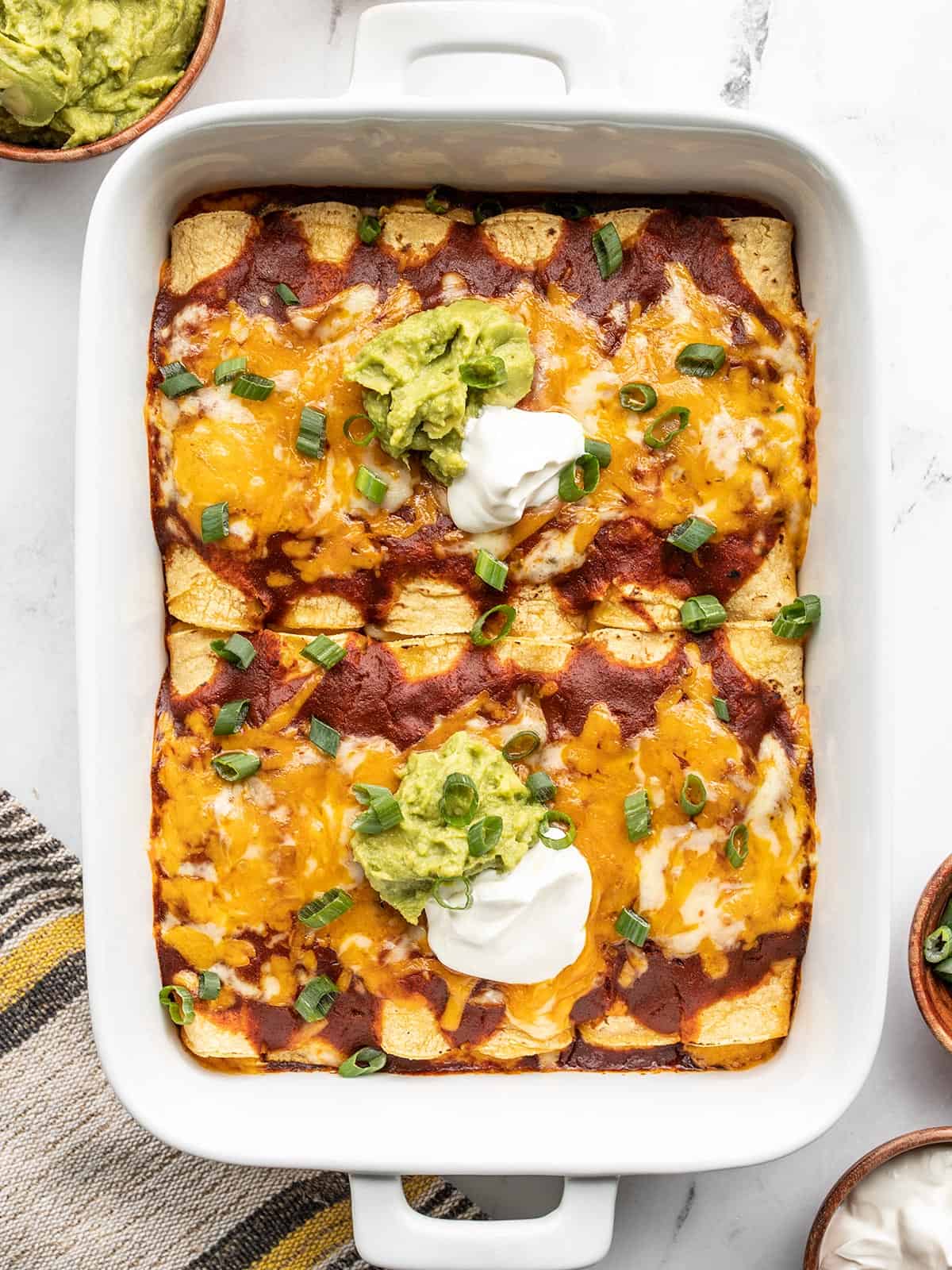 finished cheese enchiladas in the casserole dish, topped with sour cream and guacamole.