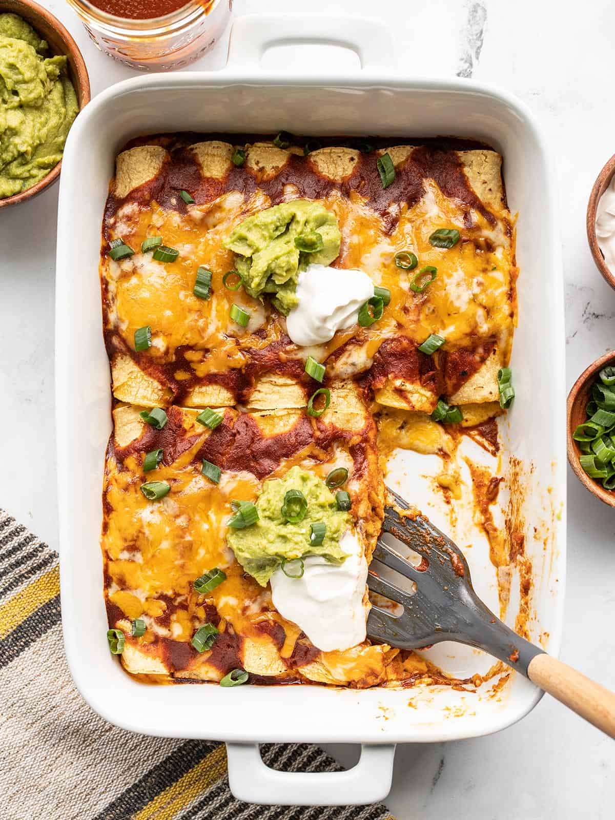 overhead view of a casserole dish full of cheese enchiladas with a spatula.