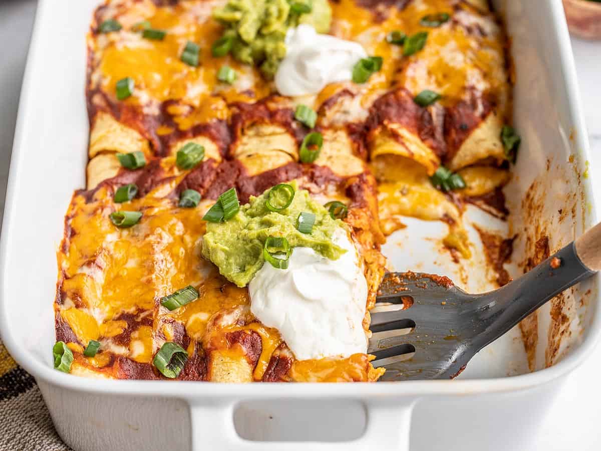 Side view of cheese enchiladas in the dish with a spatula scooping.