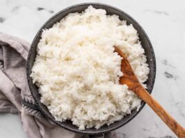 Cooked rice in a black bowl with a wooden spoon.