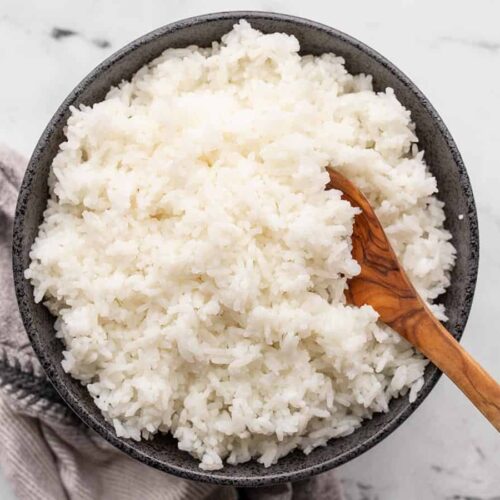 Cooked rice in a black bowl with a wooden spoon.