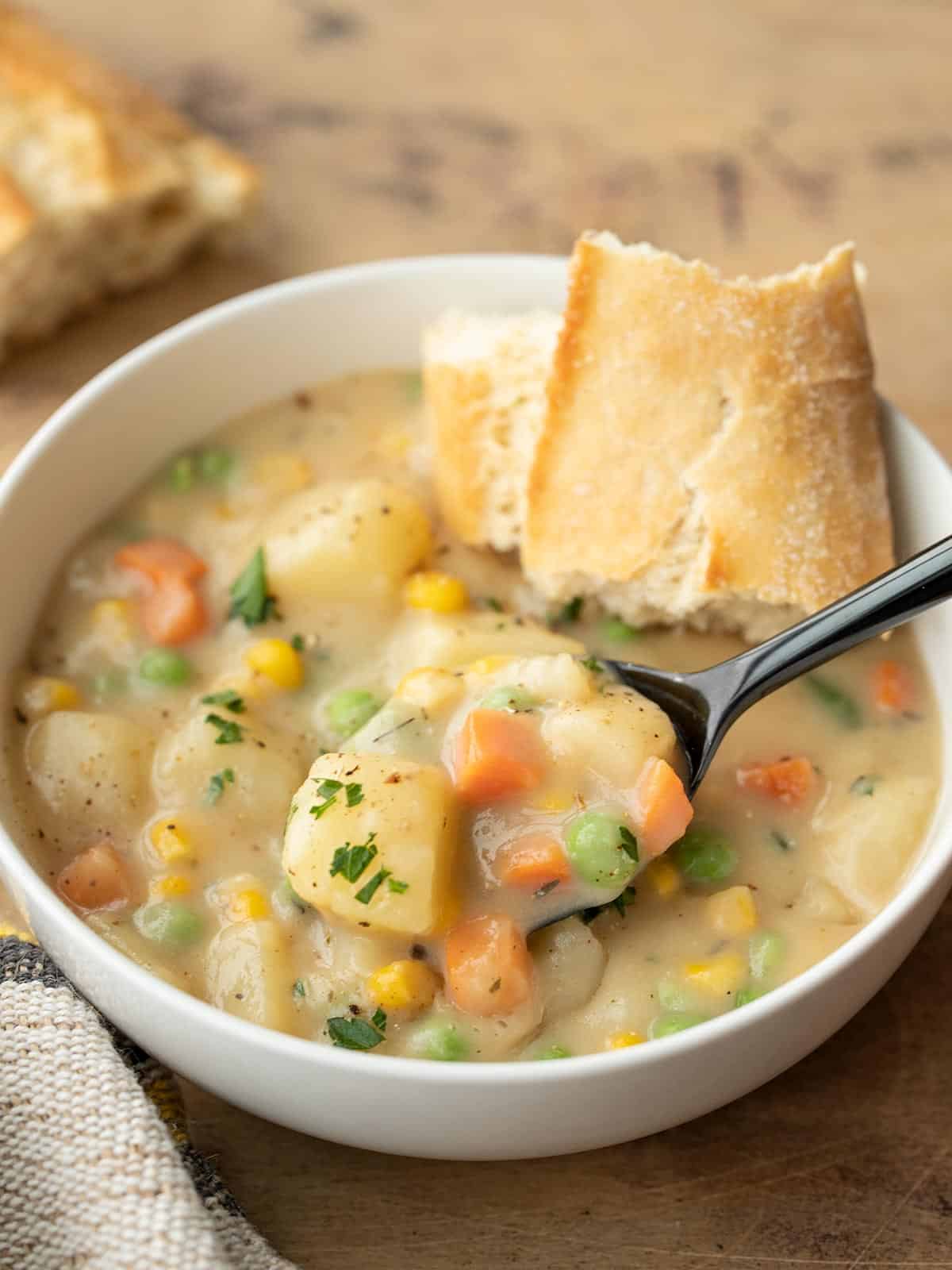 side view of a bowl of vegetables and gravy with a piece of bread and a spoon.