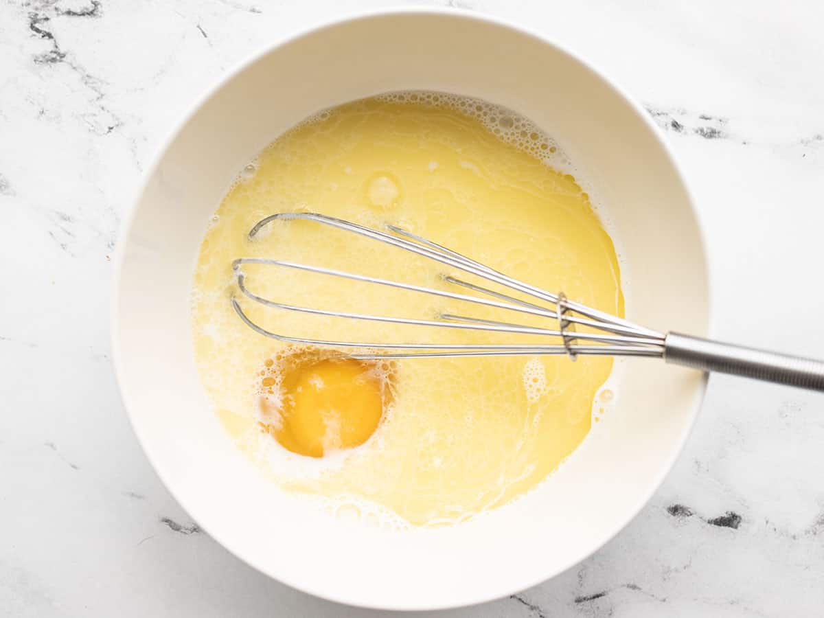 Wet ingredients for pancakes in a bowl with a whisk.