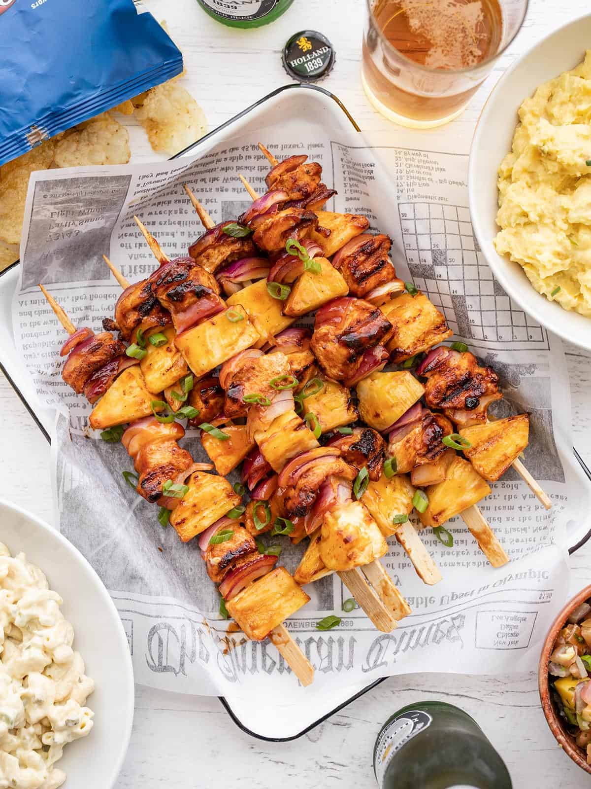 Overhead view of BBQ Chicken Kebabs on a tray surrounded by side dishes.