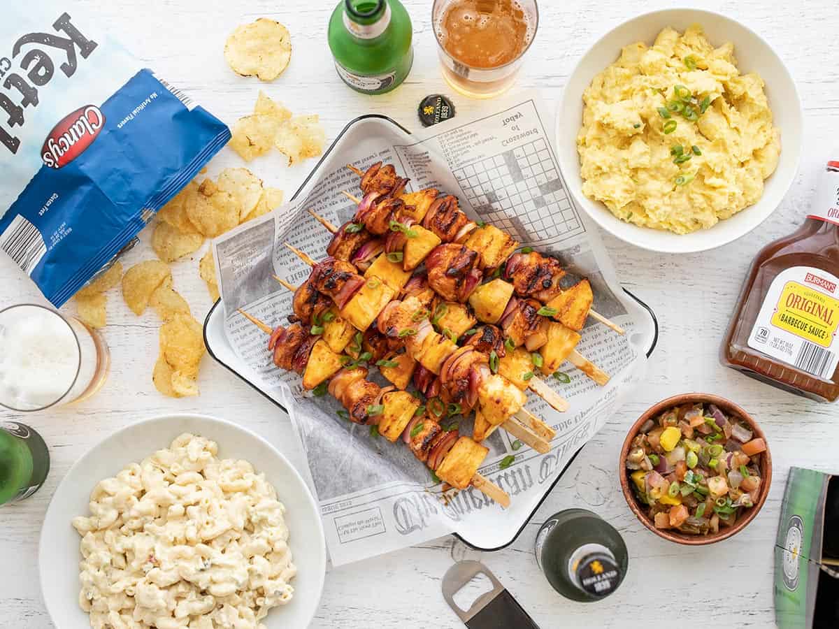 Overhead view of cooked chicken kebabs surrounded by side dishes.