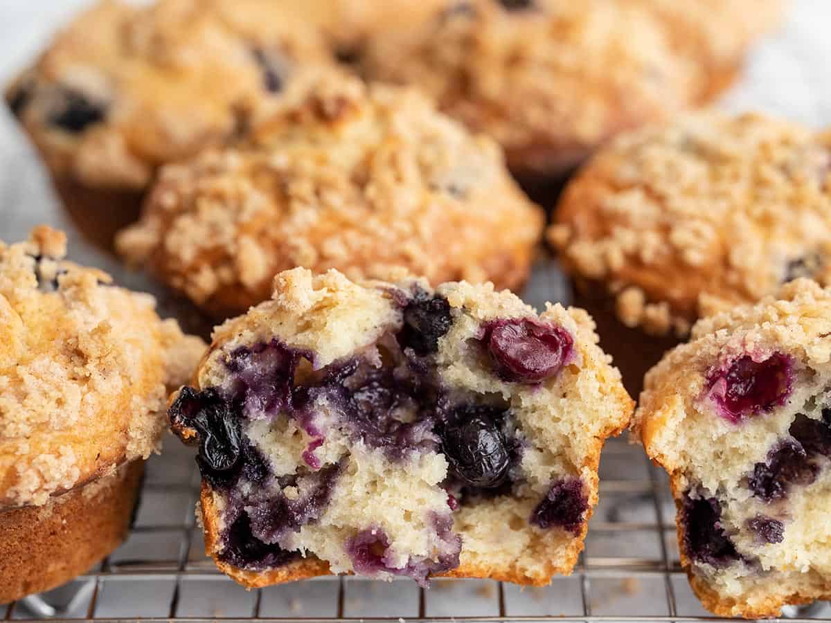 Close up side view of an open blueberry muffin next to other baked muffins.