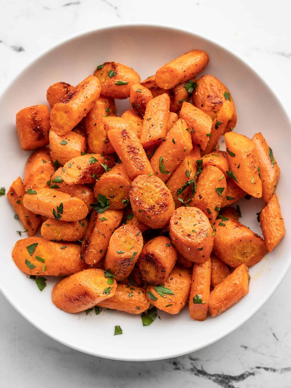 Overhead view of roasted carrots garnished with parsley in a bowl.