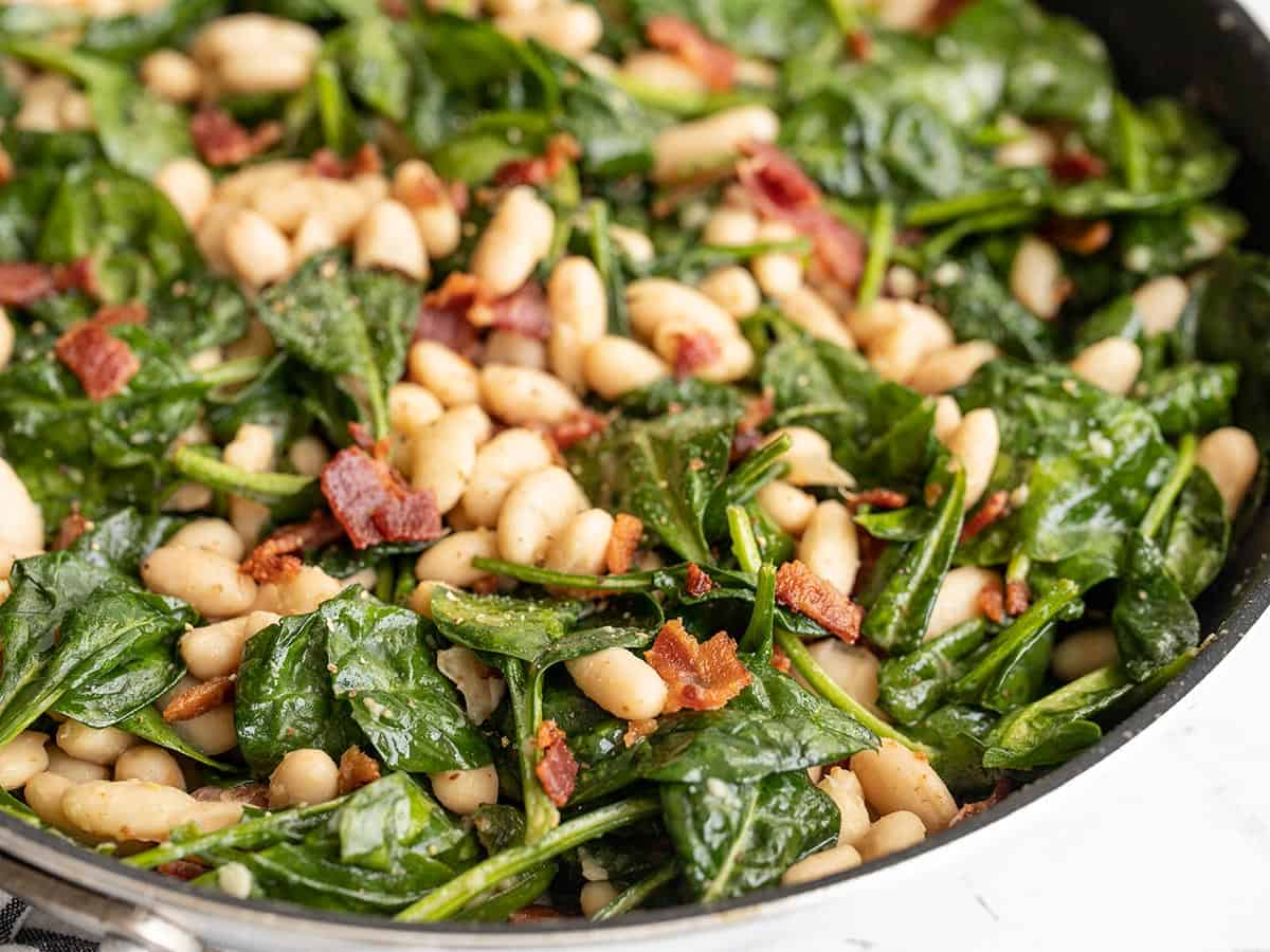 close up side view of wilted spinach salad in the skillet.