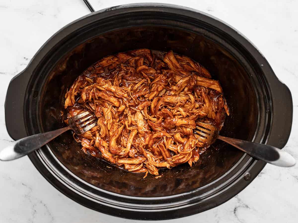 Chicken being shredded with forks in the slow cooker.